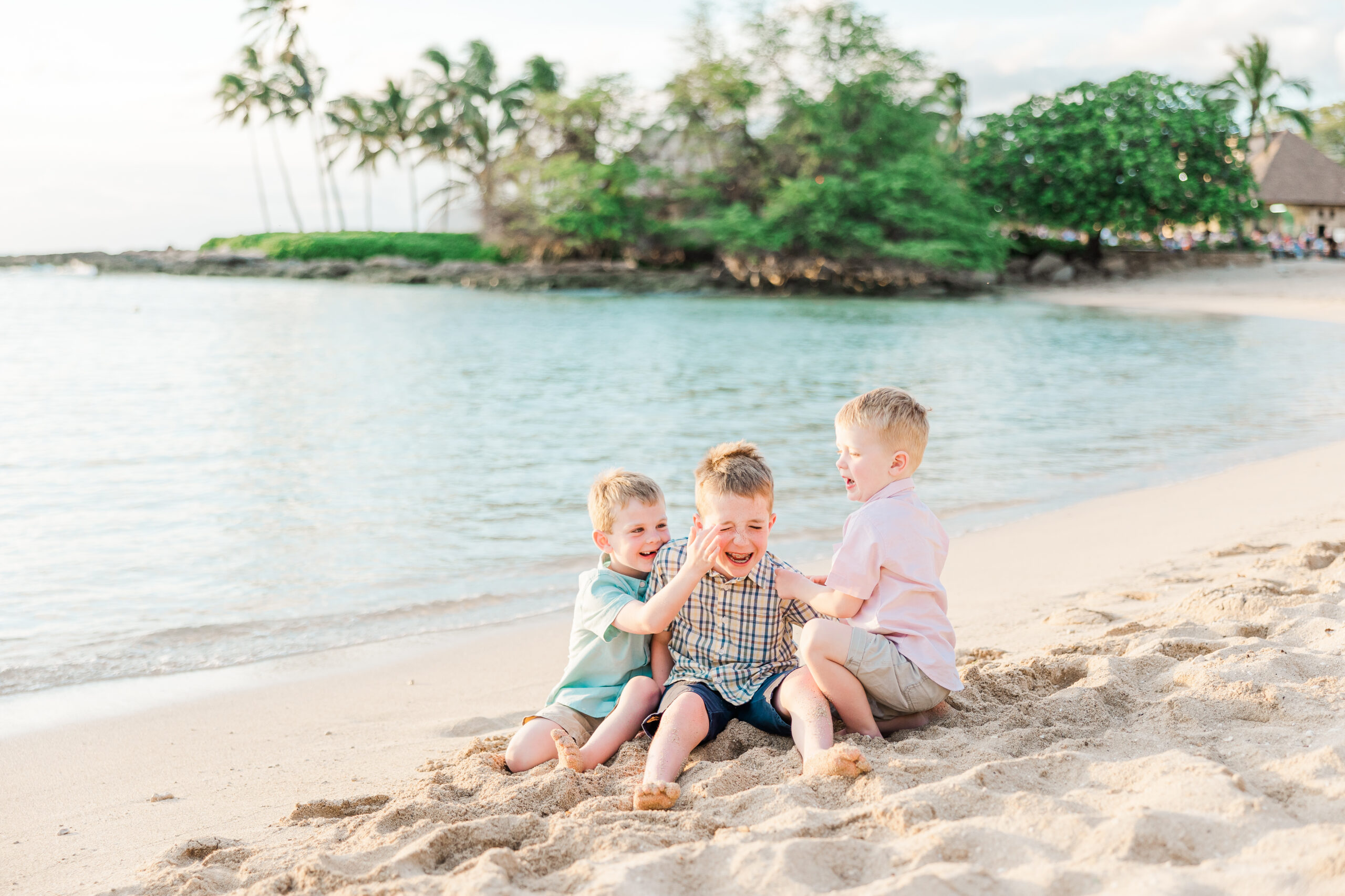 three young children tickling eachother in the sand on the beach