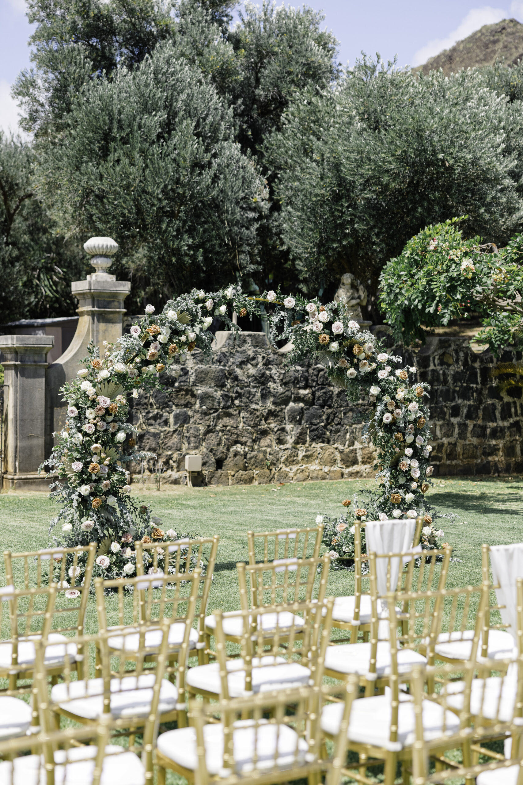 gold chiavari chairs leading to an elaborate floral arch at la pietra