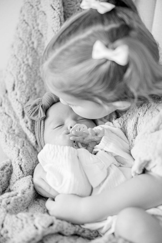 big sister kissing newborn baby sister